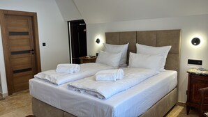 Un lit double avec du linge de lit blanc et deux serviettes enroulées, une porte en bois, une table de chevet avec une lampe et une table d’appoint en marbre.