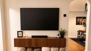 Una sala de estar moderna con una mesa consola de madera, un televisor de pantalla plana montado en la pared y cestas decorativas.
