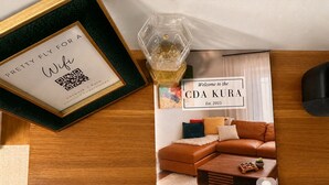 Un cartel enmarcado con un código QR y texto, un letrero de bienvenida para CDA KURA, un sofá de cuero marrón y una mesa de centro de madera.