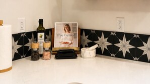 Una cocina con armarios verdes, una estufa, una encimera con saleros y pimenteros, una botella de aceite de oliva y un libro enmarcado titulado 'True Comfort'.