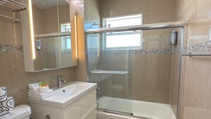 Casa de banho moderna com chuveiro em cabine de vidro, banheira, lavatório e sanita.