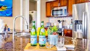 Una cucina con un piano di lavoro in granito, due bottiglie d'acqua Pellegrino, una pianta in vaso e un frigorifero in acciaio inox.