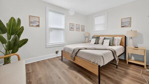 Un dormitorio con una cama de madera, una mesita de noche, una lámpara y una planta grande.