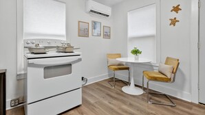 Una cocina compacta con estufa blanca, una pequeña mesa de comedor con dos sillas y una planta en maceta sobre la mesa.