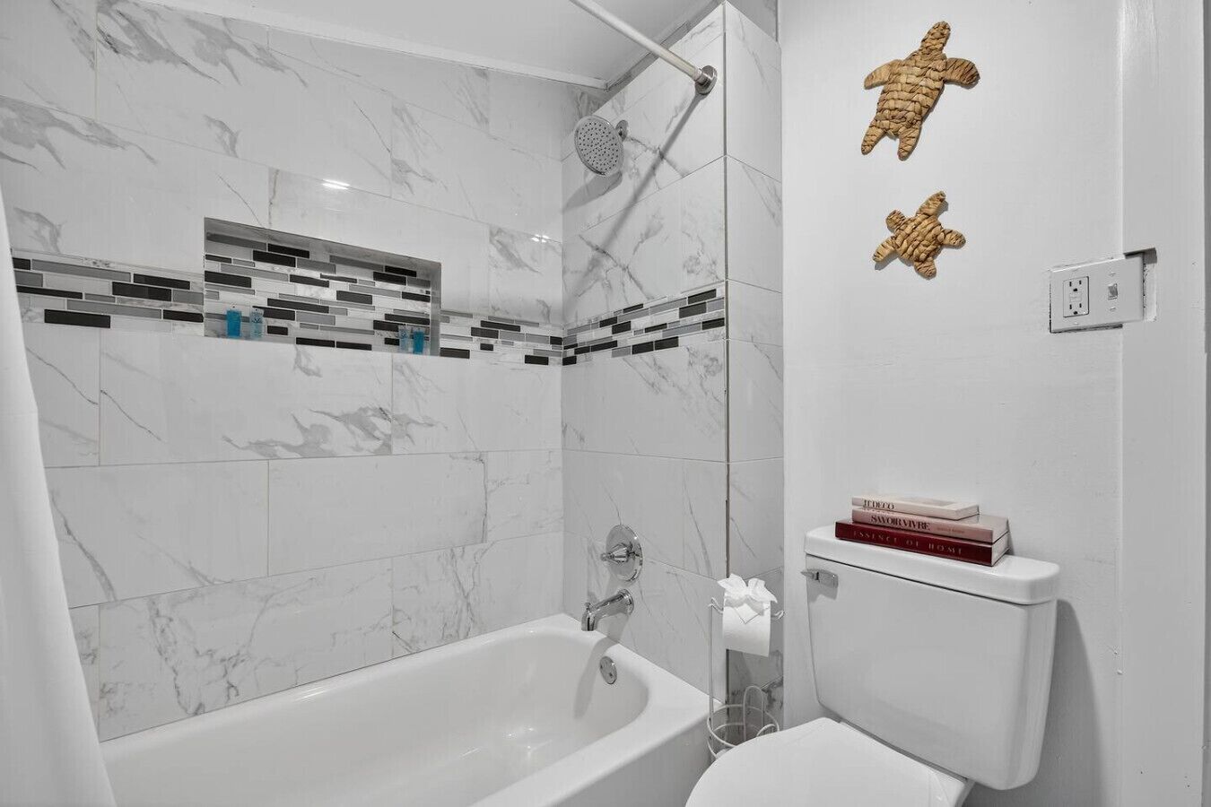 A bathroom with a bathtub, a shower, and a toilet. There are decorative tiles on the wall and a towel rack.