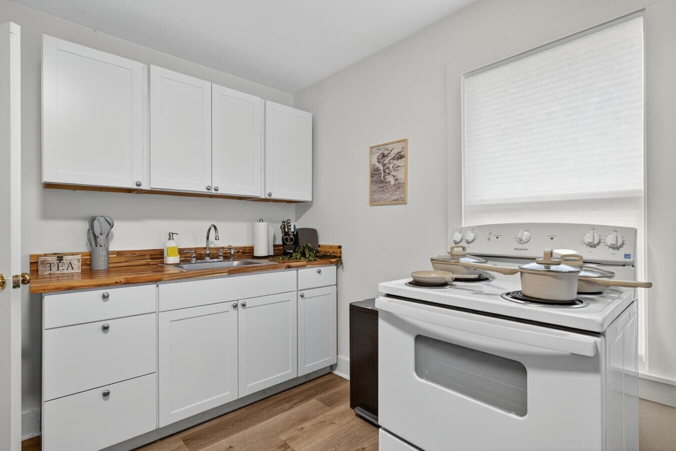 A kitchen with white cabinets, a wooden countertop, a stove, and a window with blinds.