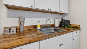 Una cocina con encimera de madera, pileta de acero inoxidable y muebles bajos blancos.