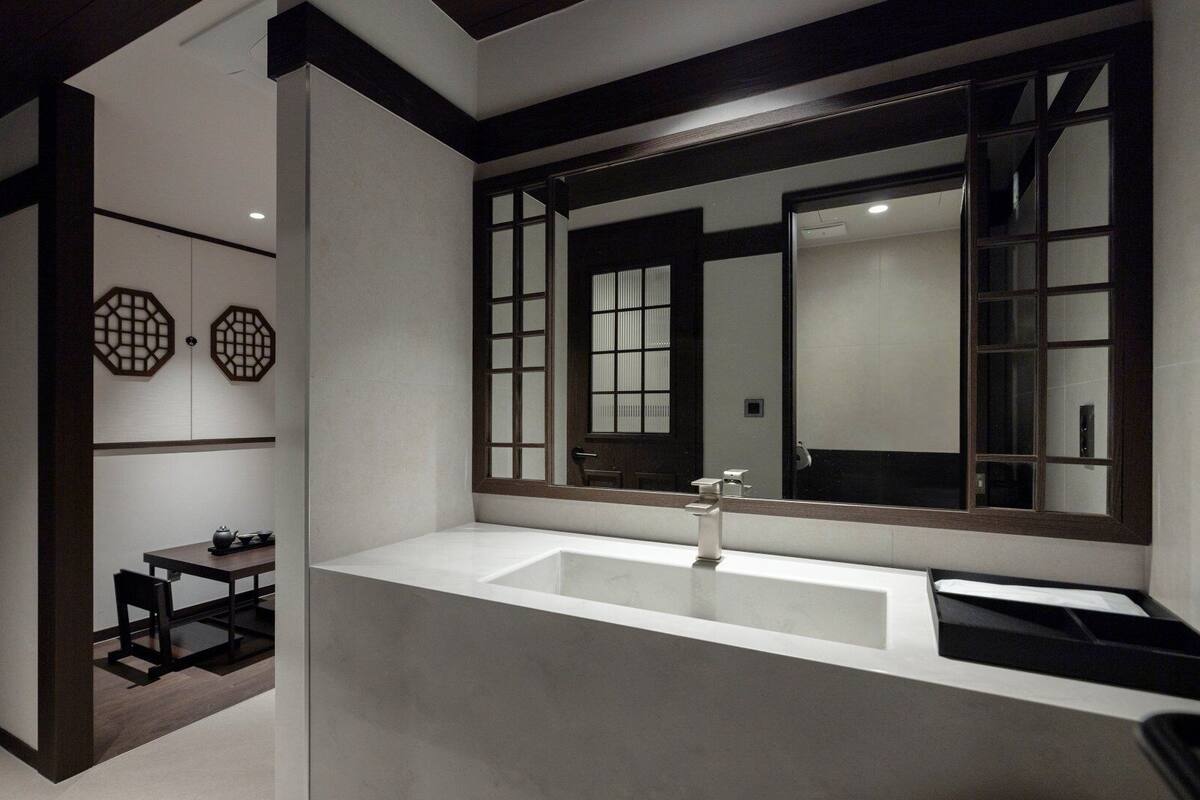 Un baño moderno con un espejo grande, un lavamanos y una mesita con un hervidor.