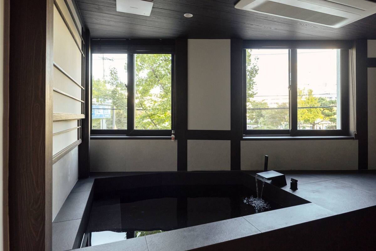 Una habitación moderna con un ventanal grande, una bañera integrada y una mesita pequeña.
