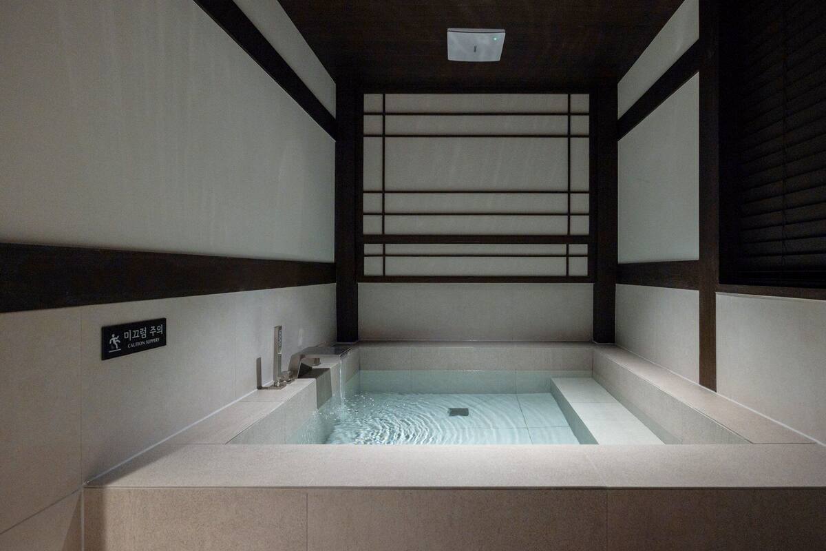 Zona pequeña y privada para jacuzzi con una señal de precaución, paredes de azulejos y techo de madera.