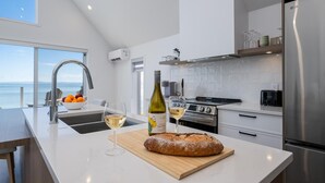 Une cuisine moderne dotée d’un grand îlot central, d’appareils électroménagers en acier inoxydable et offrant une vue sur la mer.