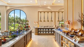 Um buffet com diversos tipos de comida, uma ilha central com pratos e luminárias pendentes.