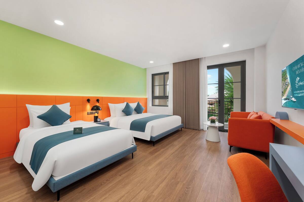Une chambre d’hôtel avec deux lits, un bureau, une chaise et une fenêtre donnant sur un espace verdoyant.