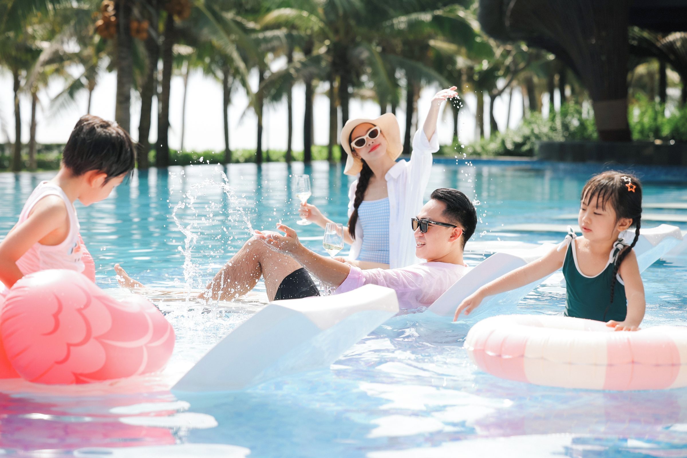 Una piscina con gente disfrutando del agua, rodeada de palmeras.