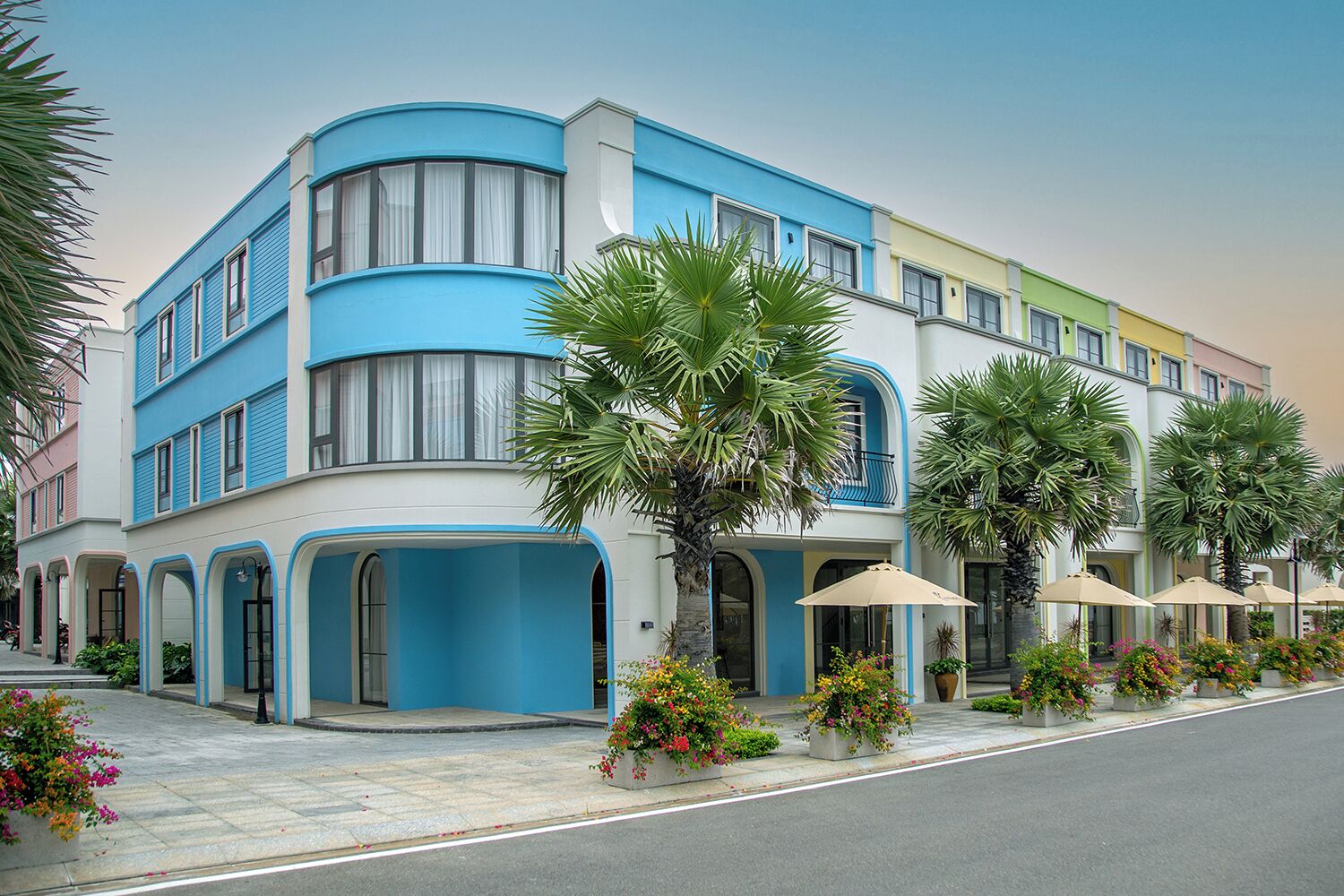 Un hôtel à plusieurs étages, doté d’une façade incurvée, de grandes fenêtres et d’un espace extérieur aménagé avec des parasols.