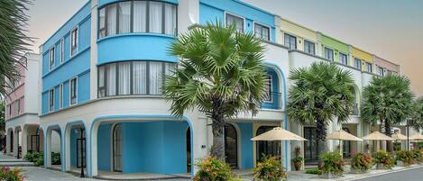 Un hôtel à plusieurs étages, doté d’une façade incurvée, de grandes fenêtres et d’un espace extérieur aménagé avec des parasols.