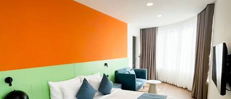 A hotel room with a large bed, a nightstand, a desk, a chair, a TV, and a window with curtains.