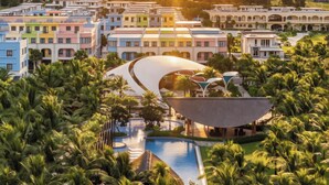 Resort com edifícios coloridos, área de piscina moderna e vegetação exuberante.