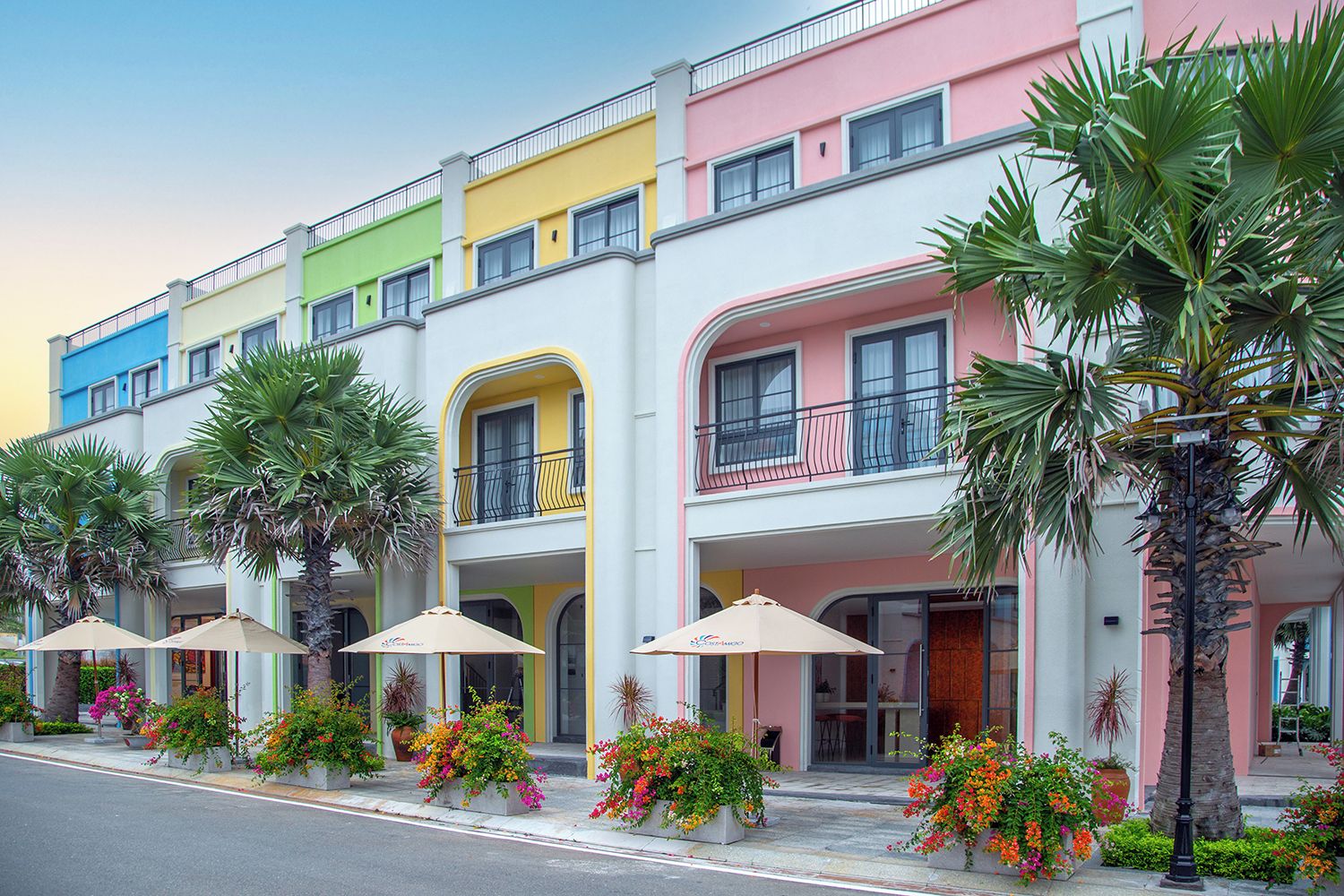 A multi-story hotel with colorful facades, balconies, and outdoor seating areas with umbrellas.