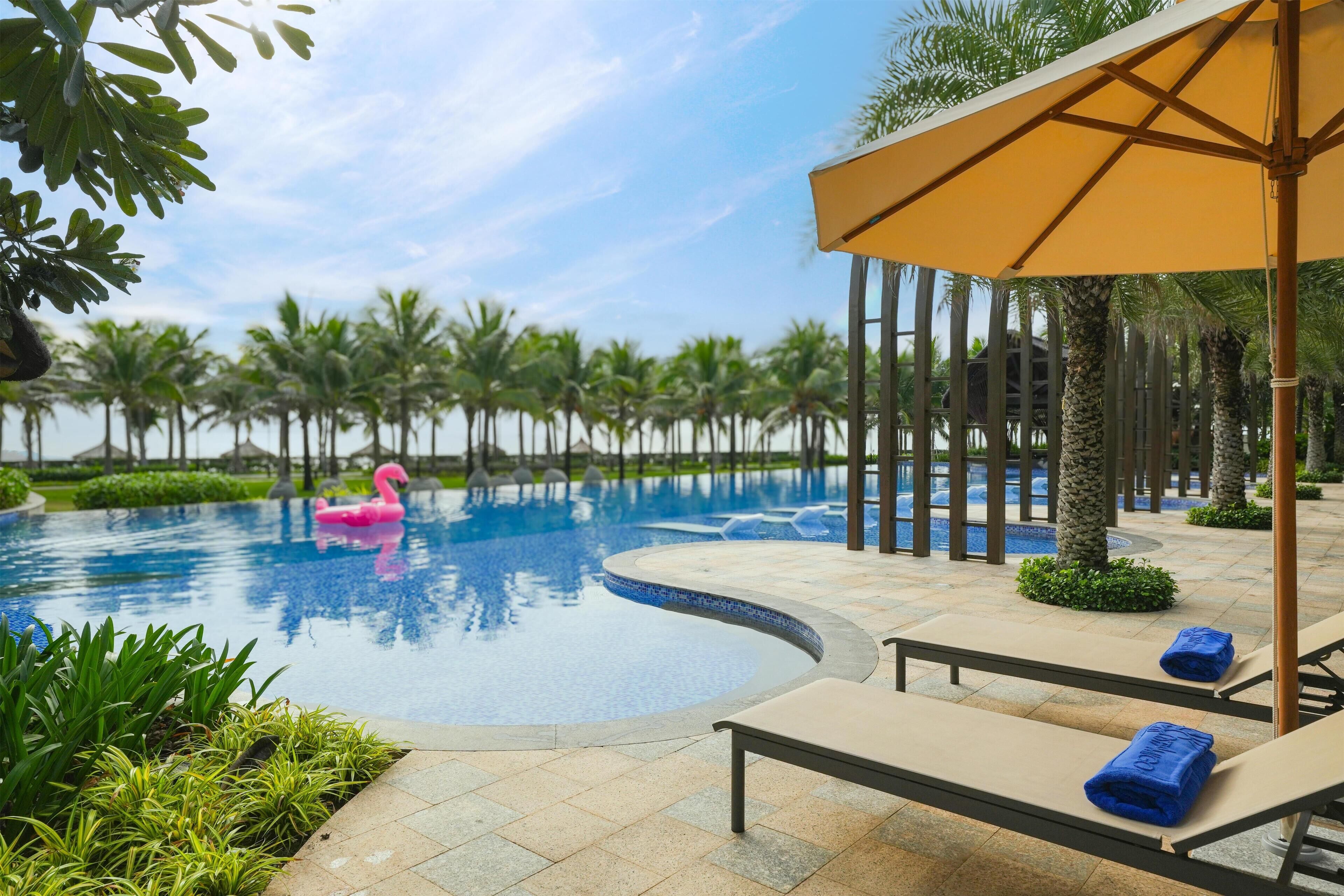 A swimming pool with a pink flamingo float, lounge chairs, and an umbrella.