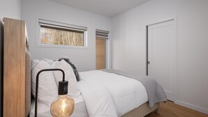 A bedroom with a bed, a wall-mounted light fixture, a window with blinds, and a door. - Panorama 1251: Private & Luxury, River Sunsets (Petite-Rivière-Saint-François)