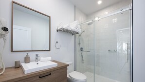A modern bathroom with a white sink, a mirror, a toilet, and a glass-enclosed shower area. - Panorama 1251: Private & Luxury, River Sunsets (Petite-Rivière-Saint-François)
