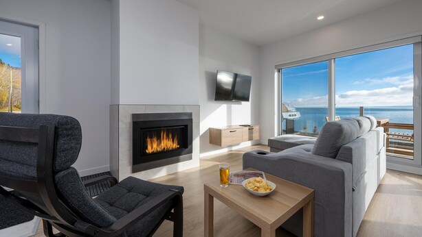 A modern living room with a fireplace, a sofa, a TV, and a view of the sea. - Panorama 1251: Private & Luxury, River Sunsets (Petite-Rivière-Saint-François)