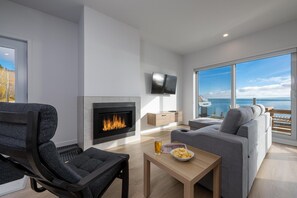 Un soggiorno moderno con camino, un divano, una TV e vista sul mare.