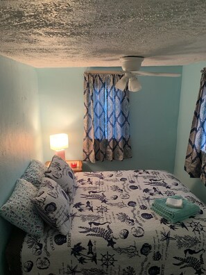 A bedroom with a bed, patterned bedding, a nightstand with a lamp, and curtains. - Pink Flamingo - Pet Friendly, Beach Side, Wi-Fi (Norfolk)