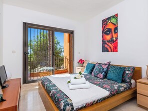Ein Schlafzimmer mit Bett, Nachttisch, Schreibtisch, einem Gemälde und einer Schiebetür zu einem Außenbereich.