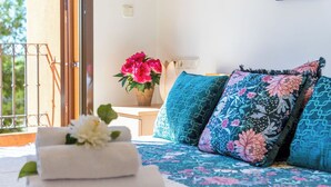 Ein Schlafzimmer mit einem Bett, Kissen, einer Vase mit Blumen und Blick ins Freie.