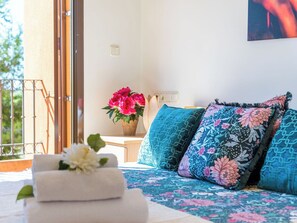 Ein Schlafzimmer mit einem Bett, Kissen, einer Vase mit Blumen und Blick ins Freie.