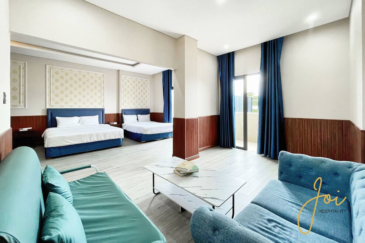 Ein Hotelzimmer mit zwei Betten, einem Schlafsofa, einem Couchtisch und einer Glastür, die auf einen Balkon führt.