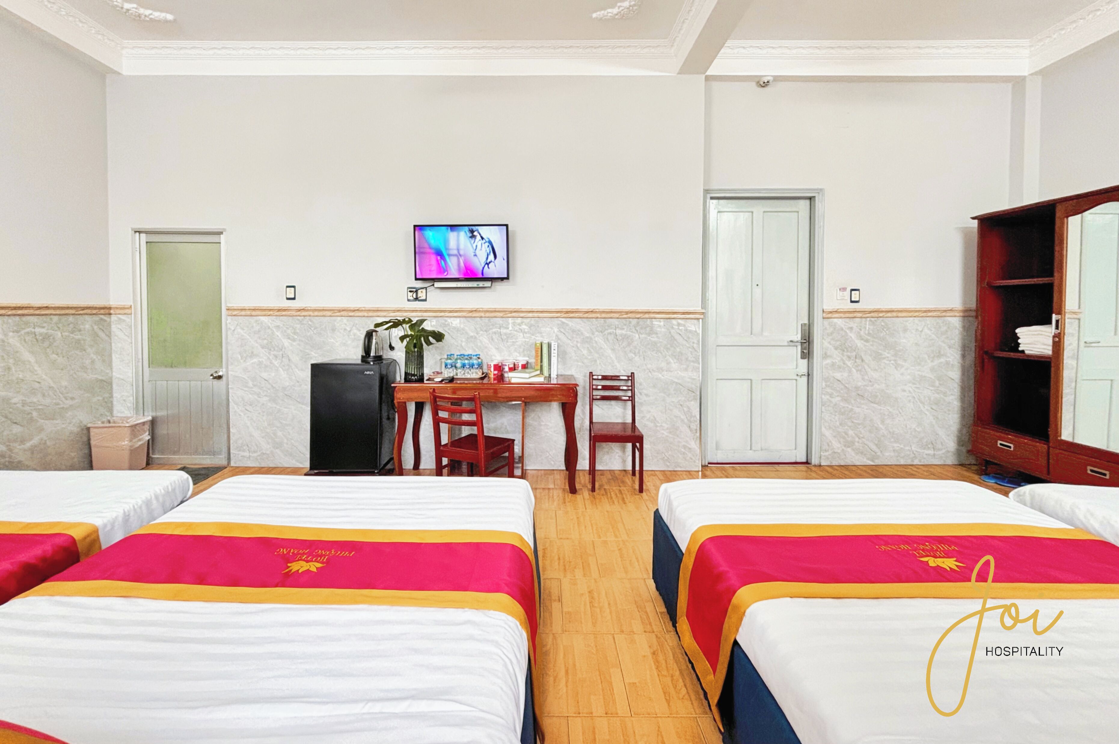 A hotel room with two beds, a desk with a chair, a television, and a wardrobe.