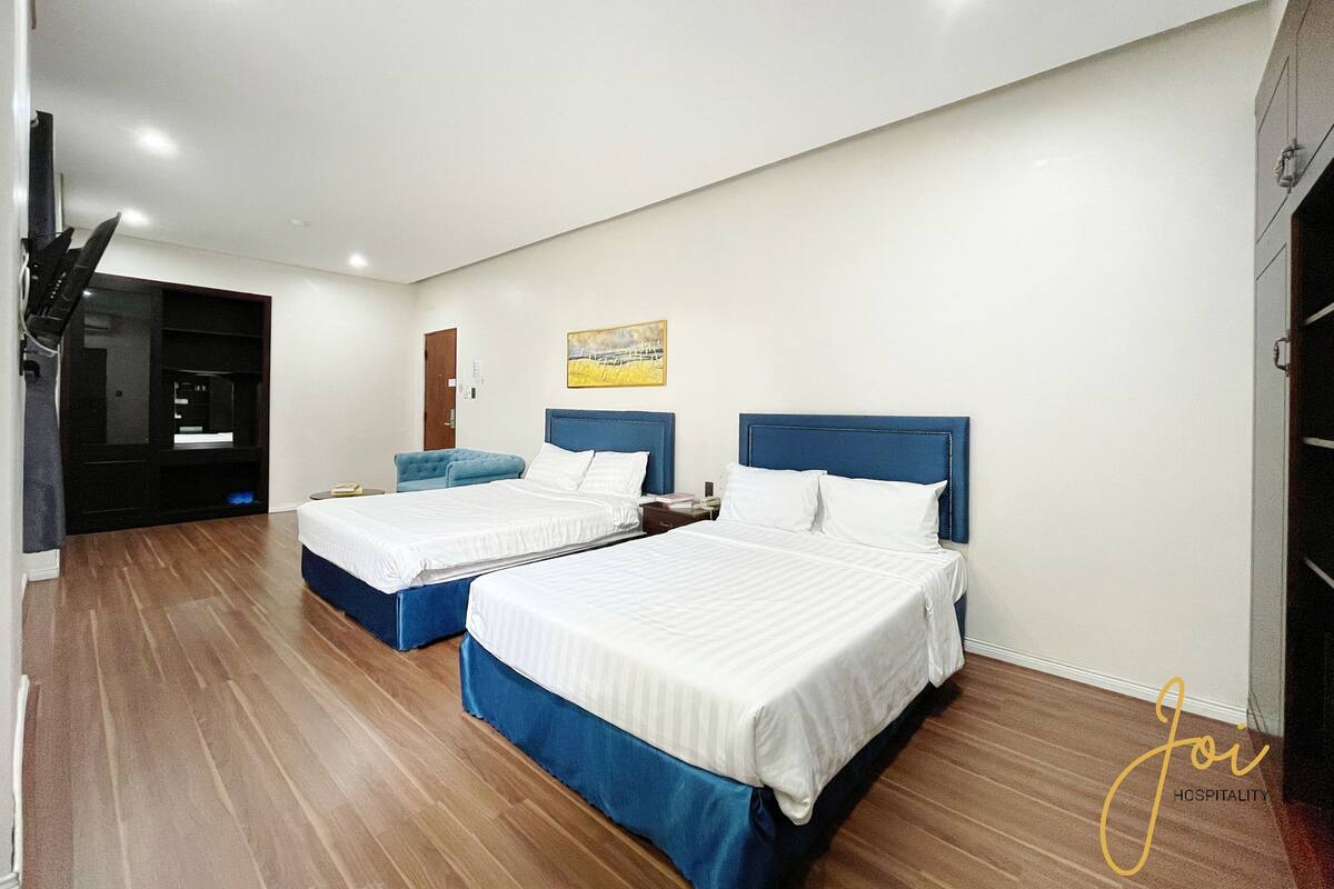 Ein Hotelzimmer mit zwei Betten, einem Flachbildfernseher, Holzboden und einem Bild an der Wand.