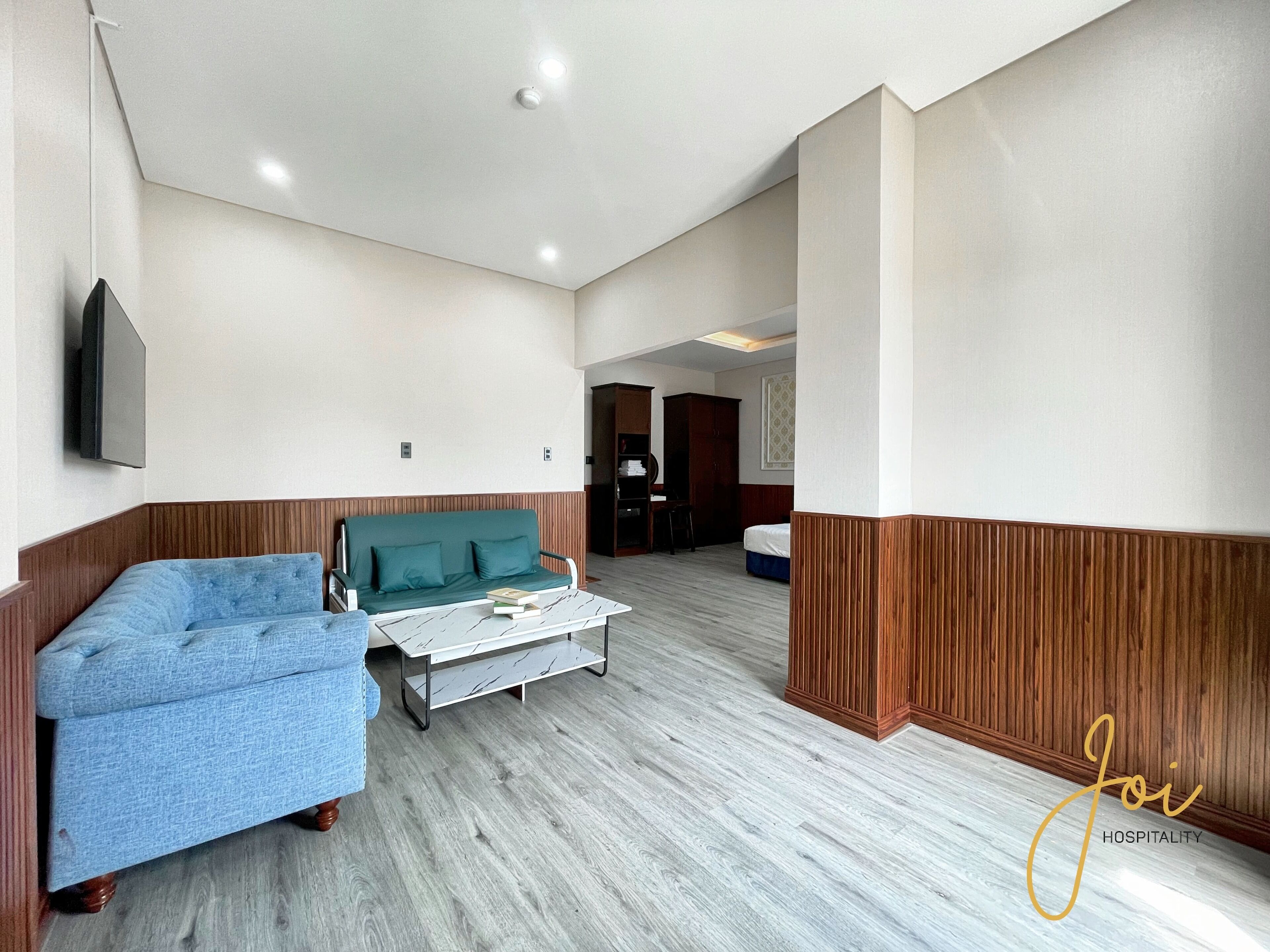 A hotel room with a sofa, a small table, a TV mounted on the wall, and a wooden accent wall.