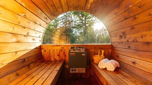 Eine Holzsauna mit Bänken und einem Steinkamin, umgeben von Blick ins Waldgebiet.