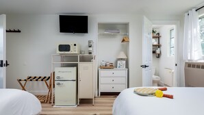 Ein Hotelzimmer mit Bett, Schreibtisch, Fernseher, Kühlschrank, Mikrowelle, einem kleinen Schrank und einem Fenster mit Vorhängen.