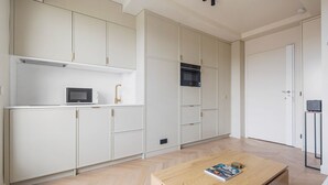 Een moderne keuken met witte kasten, een magnetron en een zwarte oven. Er staat een houten tafel met een tijdschrift en een klein voorwerp op.