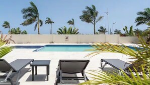 Zona de piscina con sillas de descanso, palmeras y cielo despejado.