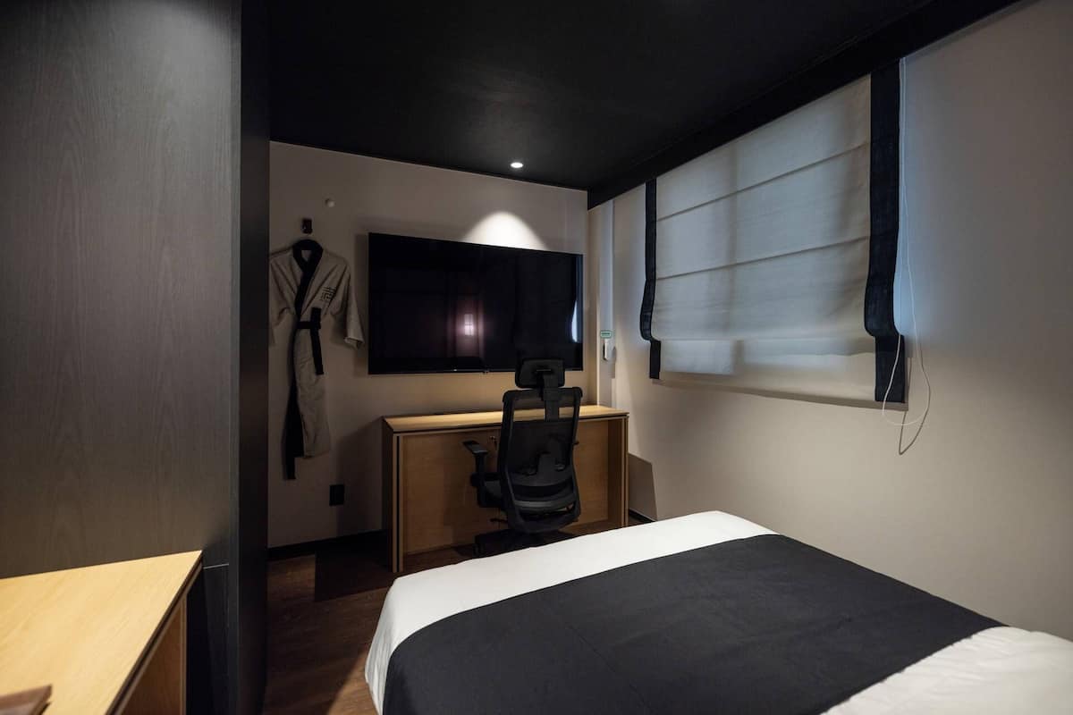 Ein Hotelzimmer mit einem Bett, einem Schreibtisch, einem Sessel, einem Fernseher und einem Bademantel, der an der Wand hängt.
