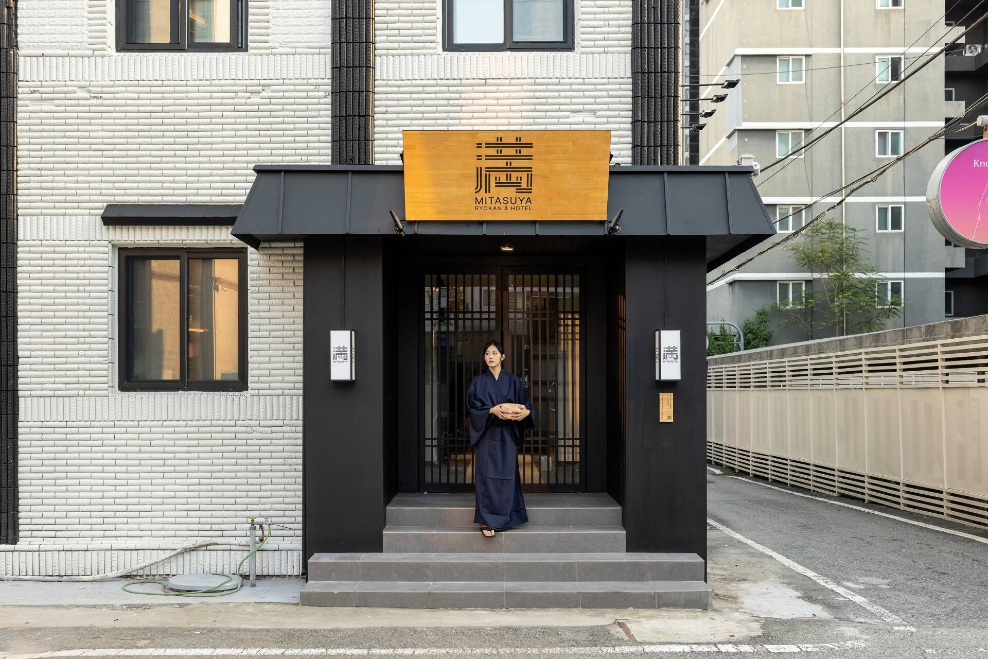 A hotel entrance with a black facade and a signboard above the door.