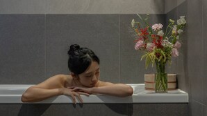 Una persona descansando en una bañera con un florero de flores en un estante.