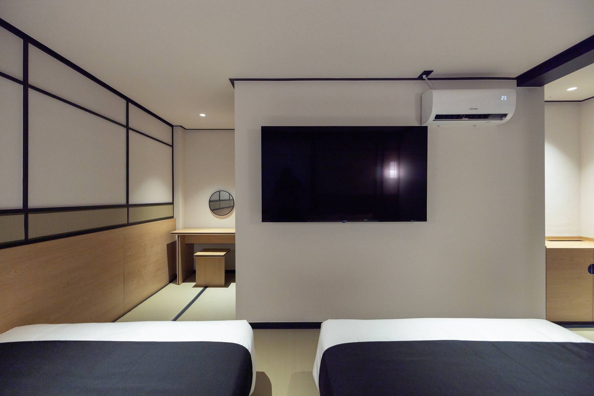 A hotel room with two beds, a TV mounted on the wall, and an air conditioning unit.