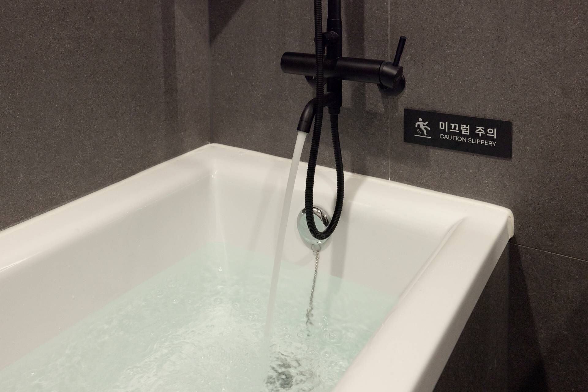 A bathtub with running water, a caution sign, and a showerhead.
