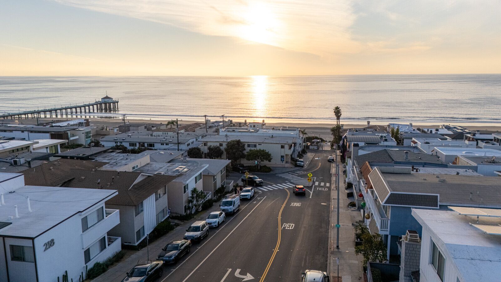A coastal urban street with a pier in the background, buildings, and parked cars.