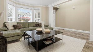 Un salon moderne avec un canapé d’angle, une table basse en verre et une grande fenêtre équipée de stores.