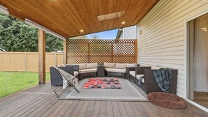 Une terrasse extérieure avec une plateforme en bois, un canapé d’angle, un foyer et un panier pour chien.