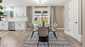 Une cuisine moderne avec des meubles blancs, un coin repas agrémenté d’un tapis à motifs et une vue sur le jardin.