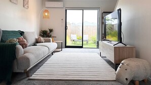 Een moderne woonkamer met een bank, een salontafel, een televisie en een schuifpui die uitkomt op een terras.